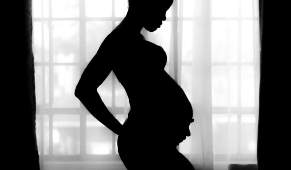 Black and white photo of pregnant woman holding her back with on hand and her belly with the other