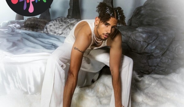 NoMBe sitting in a bed of white sheets while wearing all white.